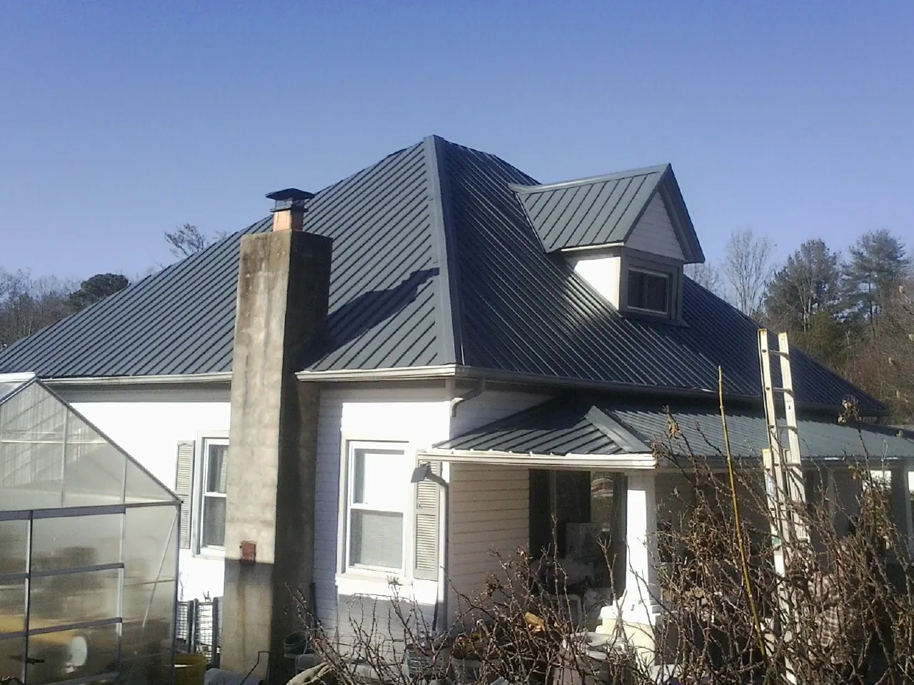 Dark blue standing seam metal roof on a white farmhouse with dormer — Slate & Tile Roof Repair by Roofing Brothers in Haslett