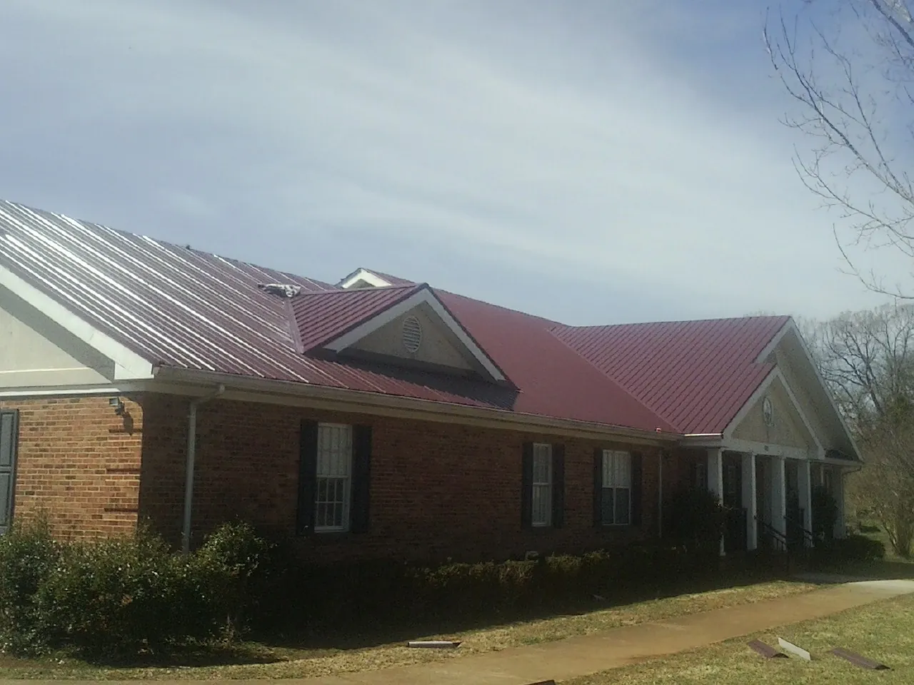 Red metal roof with gabled entries on a long brick building, from a Hail Damage Roof Repair job in Haslett