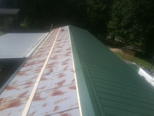 Old rusted panels beside newly installed green metal roofing — Wind Damage Roof Repair by Roofing Brothers in Haslett