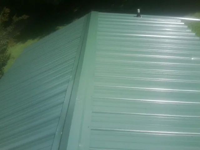 New green metal panels meeting at the ridge of a roof — Flat Roof Repair work by our crew in Haslett