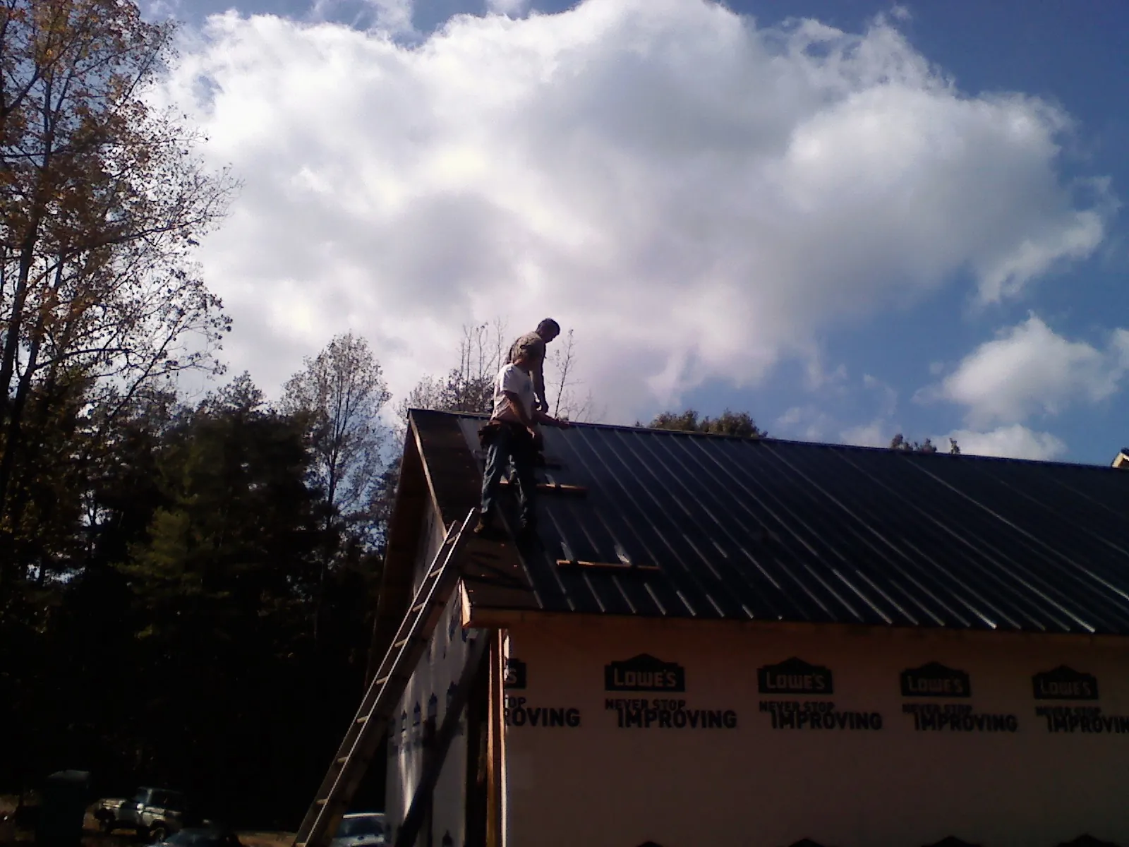 Roofer fastening dark metal panels high against a cloudy sky, from a Roof Inspection job in Haslett