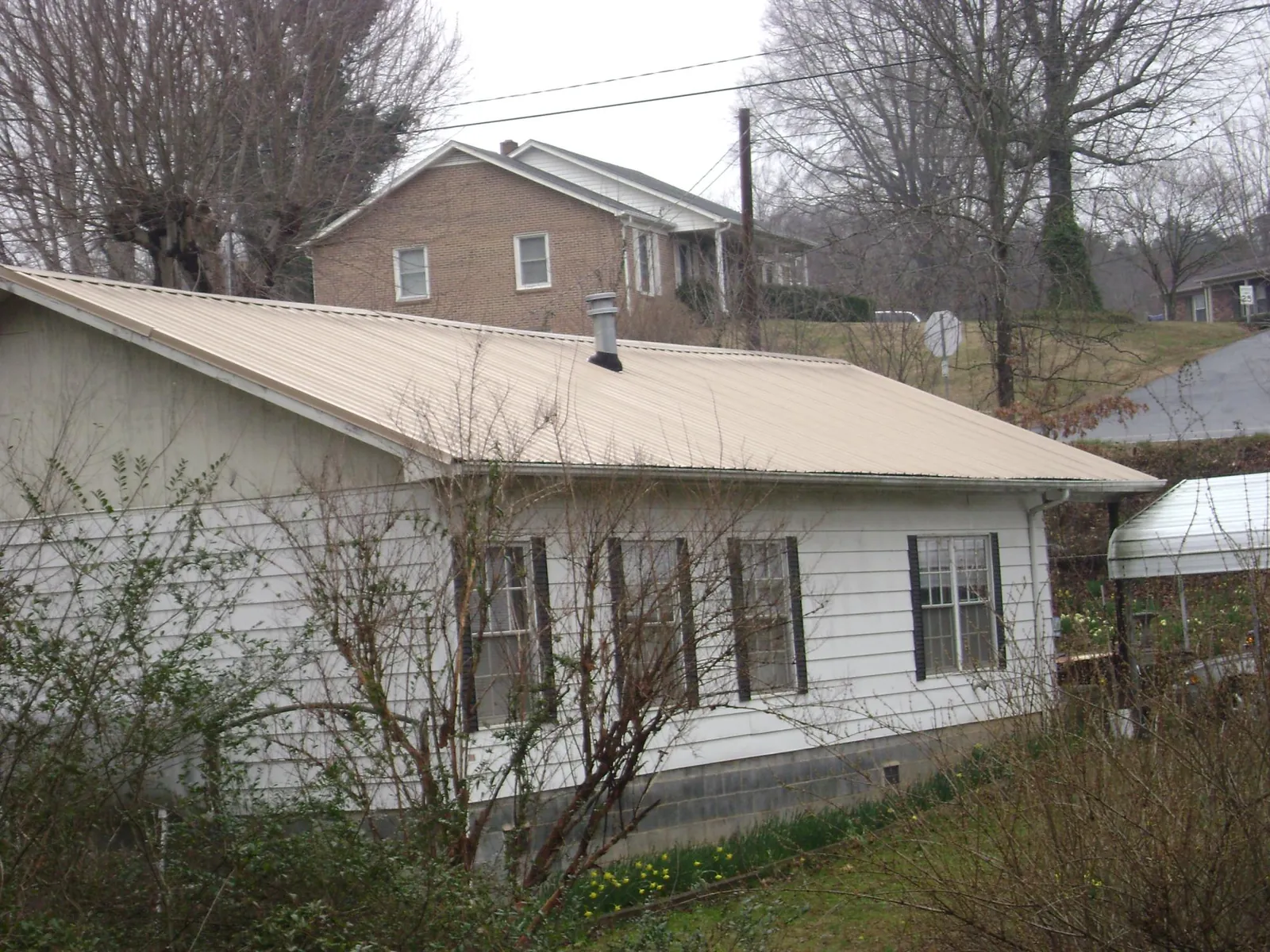 Tan metal roof on a white sided house set into a hillside — Commercial Roofing by Roofing Brothers in Haslett