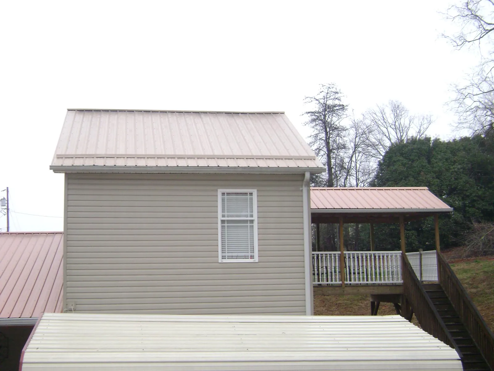 Tan metal roofs on a two story addition and attached porch, from a Roof Replacement job in Haslett