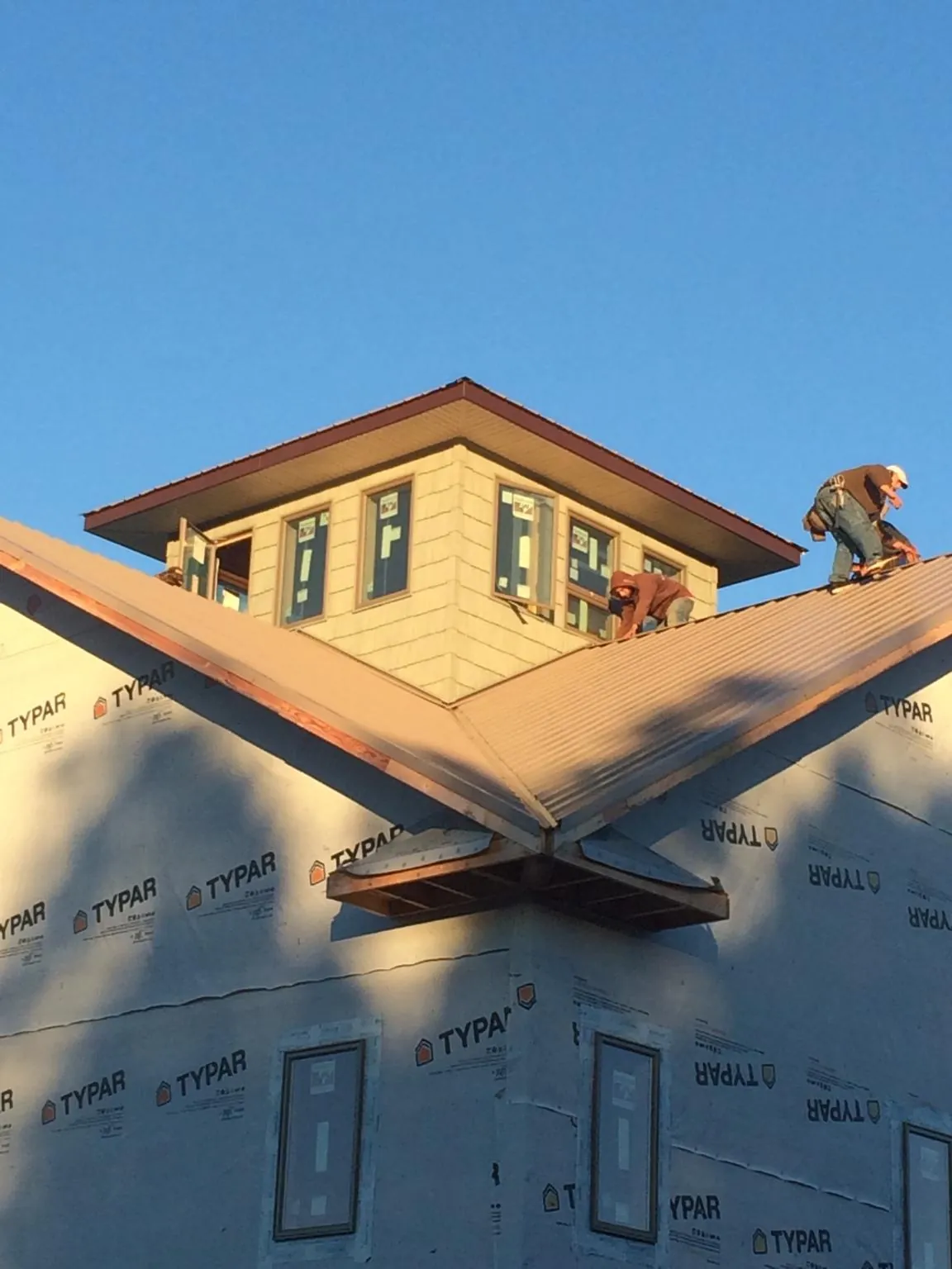 Roofers working around a rooftop cupola on a new metal roof at sunset — Roof Waterproofing in Haslett by Roofing Brothers